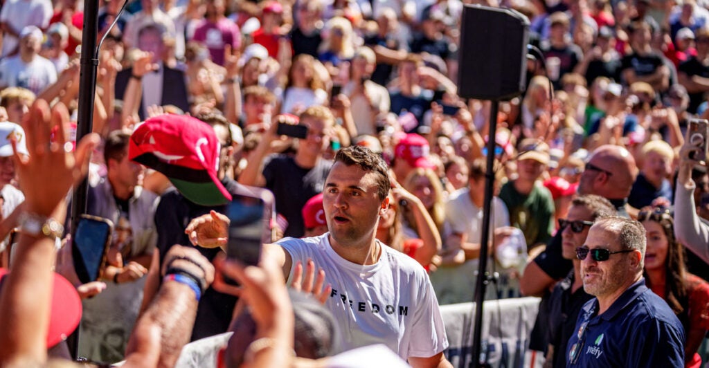 Charlie Kirk, surrounded by people, tosses a hat into crowd.