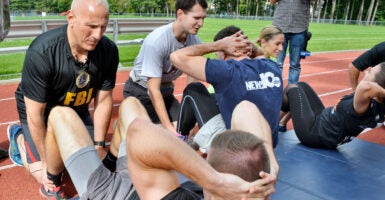 FBI trainees doing sit-ups while trainers hold their feet.