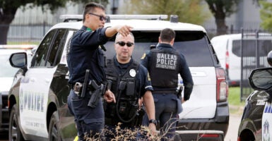 A Dallas police officer points out something to a fellow officer as another officer stands in front of a Dallas police vehicle.