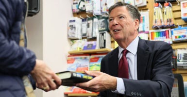 James Comey, seated, hands a copy of his book to someone during a book signing.