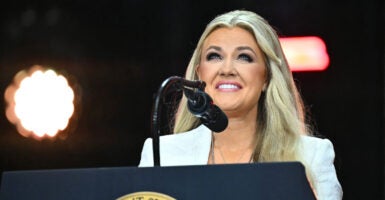 Erika Kirk, in a white outfit, smiles while standing behind a podium with the Presidential Seal.