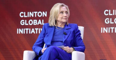 Hillary Clinton in a blue suit in front of a sign for the Clinton Global Initiative.