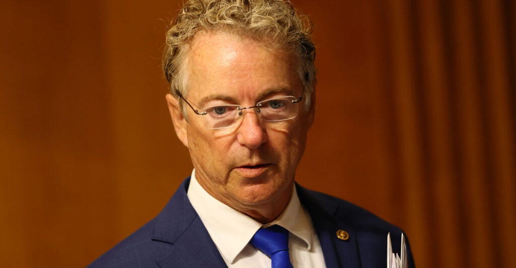 Rand Paul walks in front of an orange background.