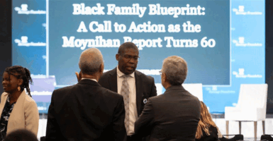 Three attendees gather to discuss in between panels in front of the stage.