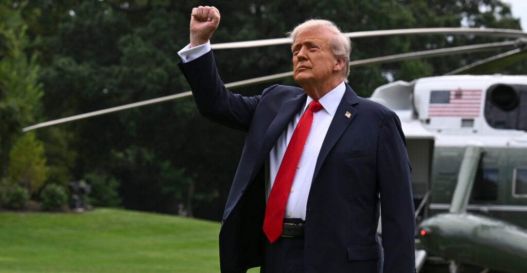 President Trump, in front of his Marine One helicopter, raises his fist.