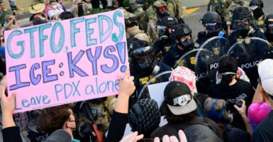 Federal agents confront protesters outside of the U.S. Immigration and Customs Enforcement building. One protest sign reads "GTFO, Feds. ICE: KYS! Leave PDX alone."