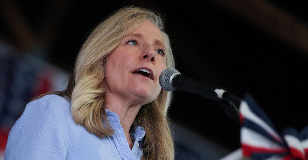 Abigail Spanberger in a blue button-down shirt speaks into a microphone at a rally