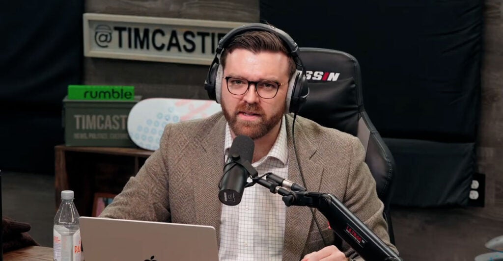 Tony Kinnett sits at the table with a microphone and his laptop on the "Timcast IRL" podcast.