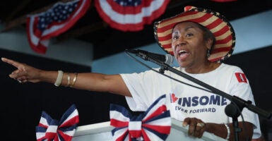 Virginia Lieutenant Governor Winsome Sears at a campaign event speaking at a podium with an American flag cowboy hat on and a T-shirt that says Winsome ever forward