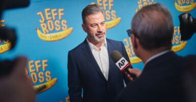Jimmy Kimmel speaks to a reporter on a red carpet with blue background.