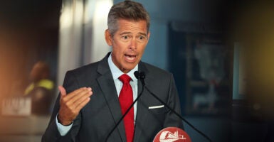 Transportation Secretary Sean Duffy in a gray suit and red tie speaking emphatically and gesturing with his hand while speaking at a podium