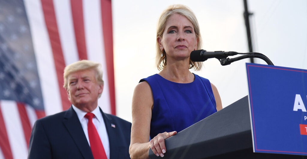 Rep. Mary Miller, R-Ill., speaks at a lectern with President Donald Trump looking on and with a U.S. flag as backdrop