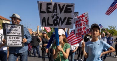 Anti-transgender protesters, including children, hold up signs that say leave us alone, we only trust our parents, and biology is not bigotry