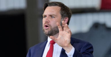 VP JD Vance in a blue suit and red tie gestures with his hand as he speaks to an audience
