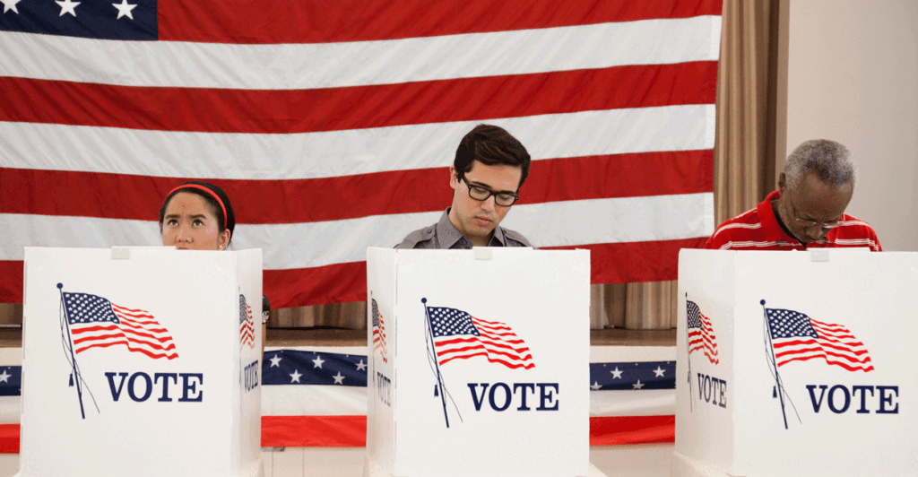 Three people voting at voting booths with an American flag as backdrop.