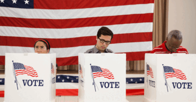 Three people voting at voting booths with an American flag as backdrop.