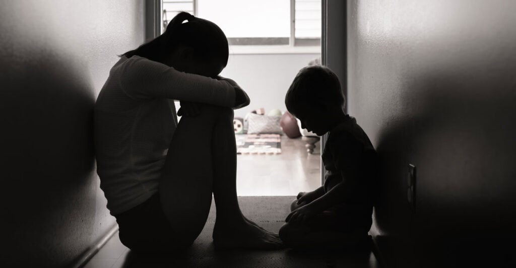 A young woman sitting on the floor of a narrow hallway with her small son with her head to her knees looking to be in despair
