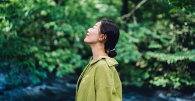 Profile shot of beautiful Asian woman in green with her eyes closed and nose up enjoying a green wooded area.