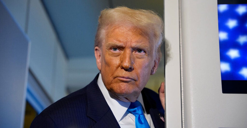 Donald Trump stands up with his head turned to his right as he listens to reporters asking him questions.