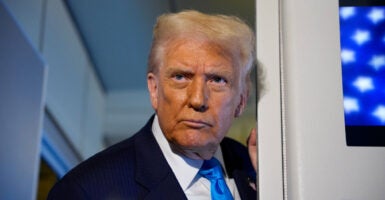 Donald Trump stands up with his head turned to his right as he listens to reporters asking him questions.