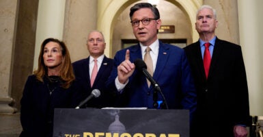 Mike Johnson stands at a podium and raises his right index finger as he speaks.