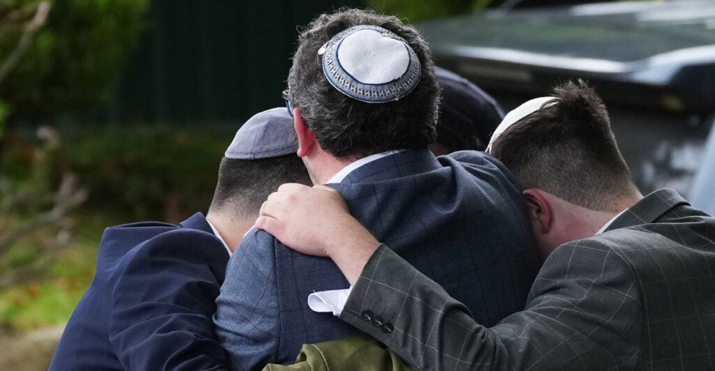 Four people form a circle as they hug each other in grief after their house of worship was attacked.