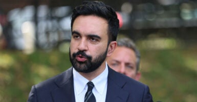 Zohran Mamdani stands outside at a press conference and looks to his right while answering questions.