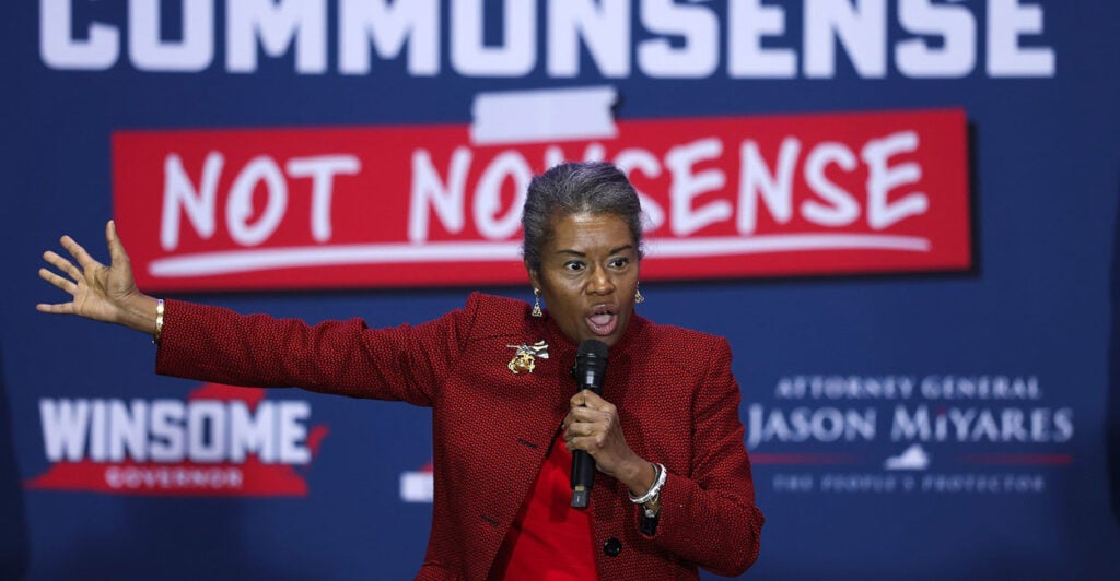 Winsome Earle-Sears stands on a stage holding a microphone in her left hand and extending her right arm out as she talks.