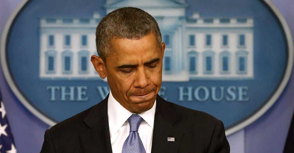 Barack Obama, with pursed lips and looking down, stands at White House press room podium.
