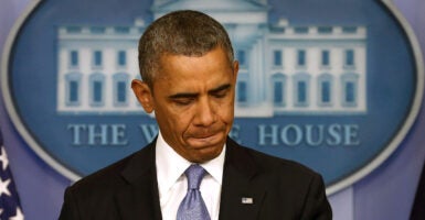 Barack Obama, with pursed lips and looking down, stands at White House press room podium.