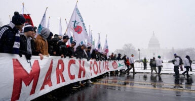 Young people carry the March for Life banner, with the U.S. Capitol in the background on a cold, snowy day.
