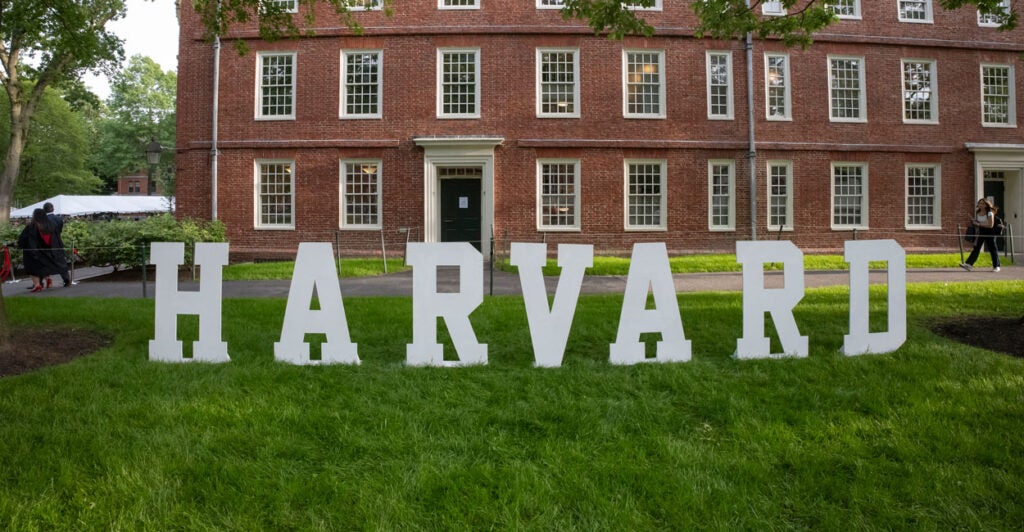 White letters spelling out "Harvard" on grass in front of a brick building.