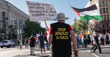 Man in black shirt with gold lettering reading "Stop Genocide in Gaza" and holding a sign walks down a Washington, DC street turning pro-Palestinian protest.