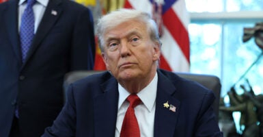 President Donald Trump in a dark blue suit and red tie sitting at his desk in the Oval Office.