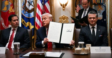 Flanked by Secretary of State Marco Rubio (left) and Secretary of War Pete Hegseth (right), President Donald Trump holds up signing documents recognizing days honoring Leif Erikson and Christopher Columbus.