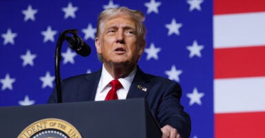 President Donald Trump at a podium, backed by a large American flag.