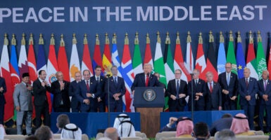 President Trump backed by international leaders and a row of international flags and backdrop reading "Peace in the Middle East," speaks.
