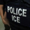 Back of an ICE agent in black uniform reading "Police ICE" in white lettering.