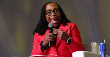 Justice Ketanji Brown Jackson in a red jacket and pants sitting in a white chair, speaks.
