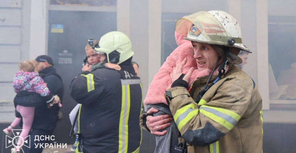 Emergency workers hold children in pink while evacuating a Ukrainian kindergarten.