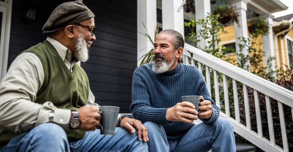 Two middle-aged neighbors, one black, one white, share coffee on a porch.