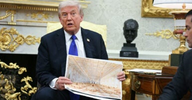 Donald Trump in Oval Office, holding up drawing of White House ballroom.