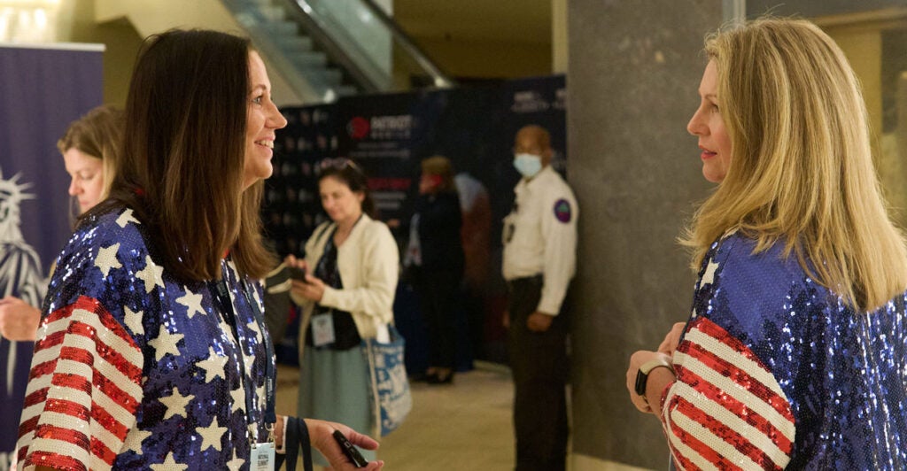 Two women dressed in glittery American flag blouses talk at the 2024 Moms for Liberty Summit.