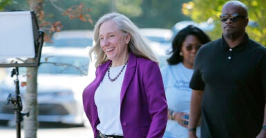 Democrat Abigail Spanberger smiles while wearing a white blouse with a blue sport coat in front of cars.