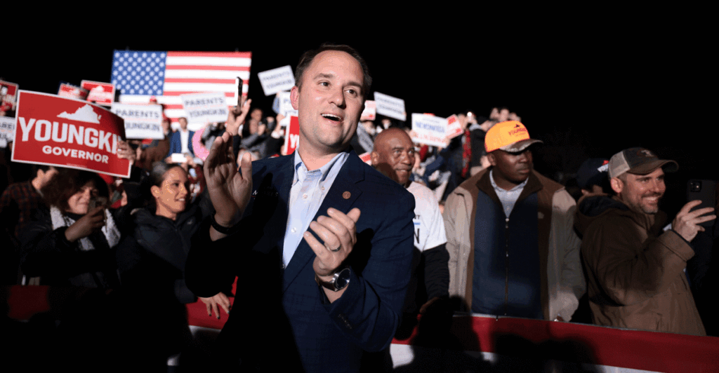 Jason Miyares clapping at a nighttime rally in front of a crowd.