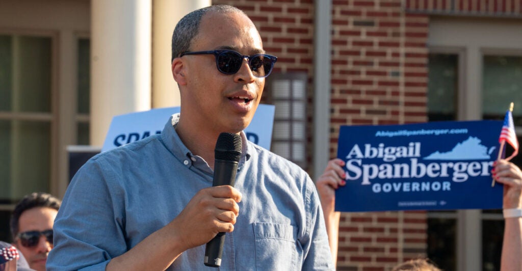 Democrat Virginia attorney general candidate Jay Jones in a blue button-down shirt with sunglasses on holding a microphone and speaking outdoors to supporters