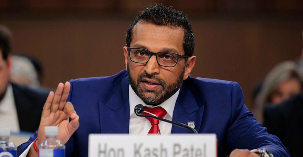 FBI Director Kash Patel, in a blue suit, makes the "OK" sign