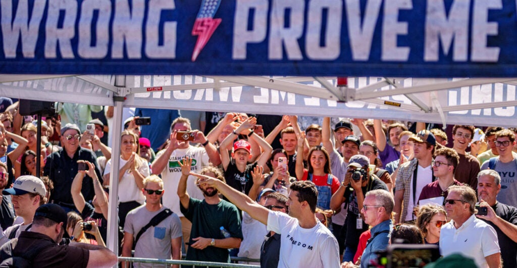 Charlie Kirk gestures as he stands under a "Prove Me Wrong" banner at Utah Valley University.