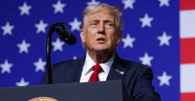 Donald Trump in a blue suit with a red tie in front of an American flag
