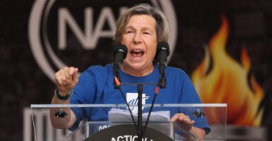 Randi Weingarten in a blue shirt stands in front of an image of fire.